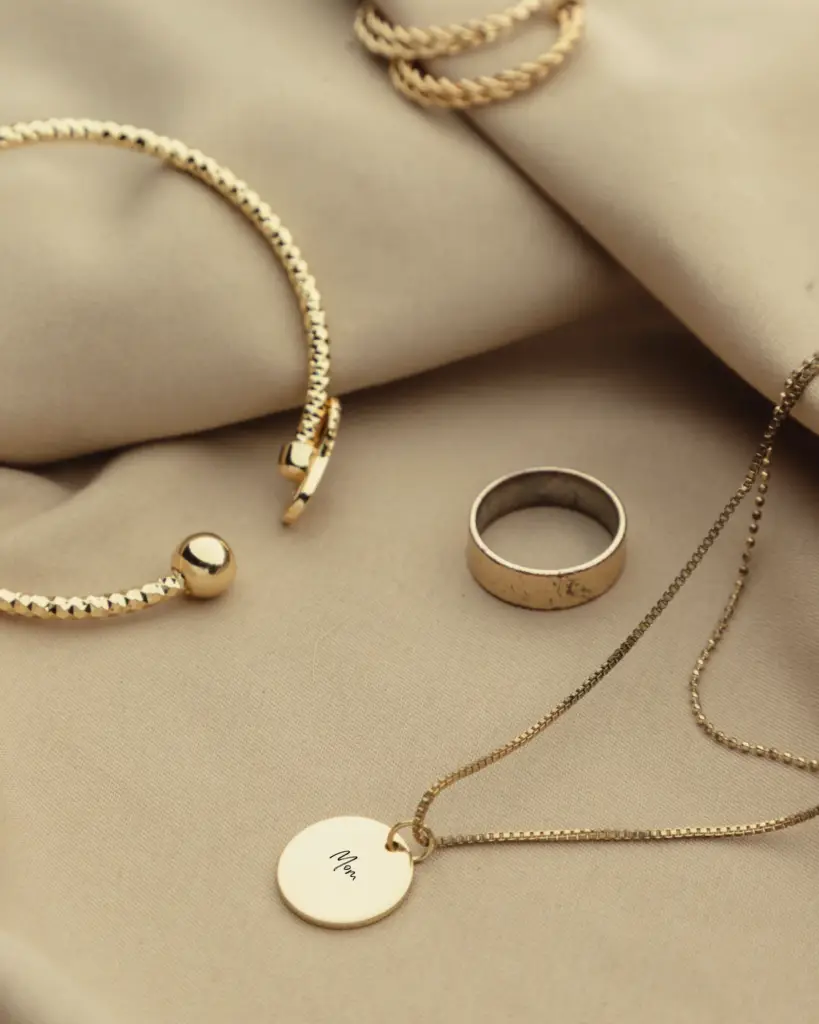 A gold necklace, ring and bracelet on top of a cloth.